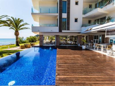 Moderner Pool mit blauem Wasser neben Holzterrasse und Meerblick, Palmen im Hintergrund.