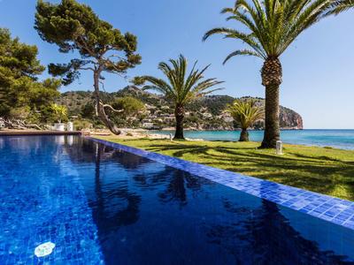Blauer Pool mit Blick auf Palmen, Rasen und Meer an einem sonnigen Tag.