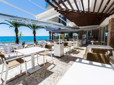 Terrasse eines Restaurants mit Blick auf das Meer, weiße Tische und Stühle unter blauem Himmel.