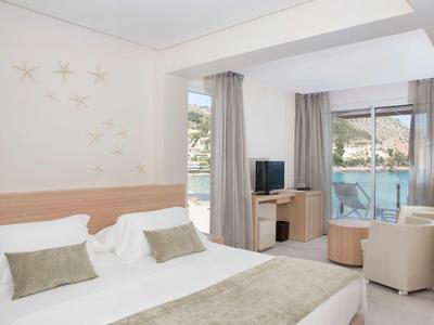 Jasny pokój hotelowy z podwójnym łóżkiem, telewizorem, miejscem do siedzenia i balkonem z widokiem na morze.