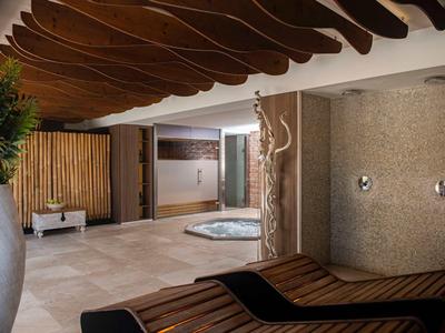 Nowoczesna strefa wellness z drewnianym sufitem, jacuzzi i strefą relaksu w ciepłych odcieniach.