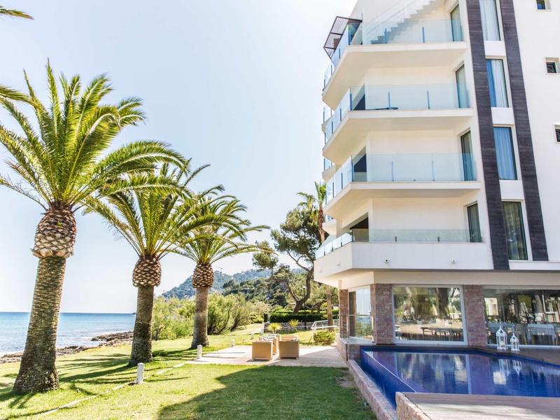 Nowoczesny hotel z palmami, basenem i widokiem na morze pod czystym niebem.