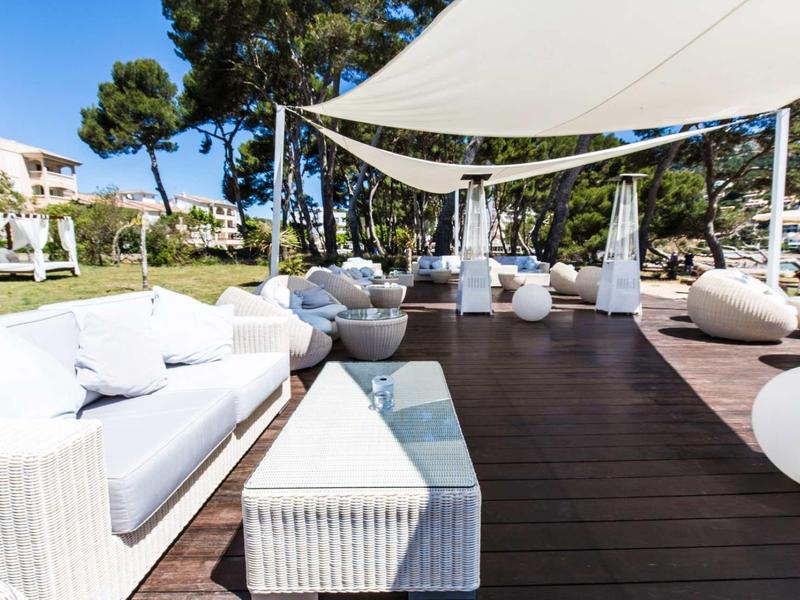 Nowoczesna przestrzeń na zewnątrz z białymi meblami lounge i daszkiem przeciwsłonecznym obok zielonego trawnika.