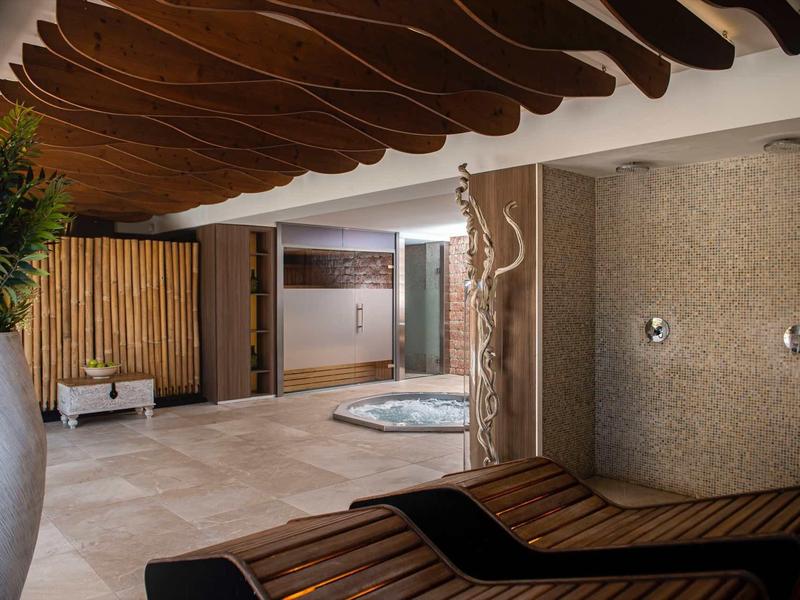 Nowoczesna strefa wellness z drewnianym sufitem, jacuzzi i strefą relaksu w ciepłych odcieniach.