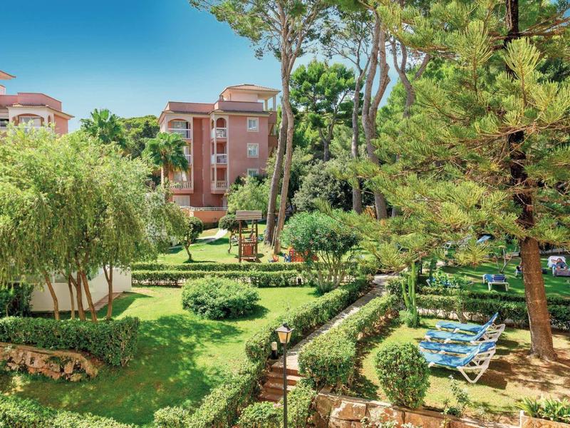 Espace jardin vert avec des arbres et des chaises longues devant plusieurs immeubles.