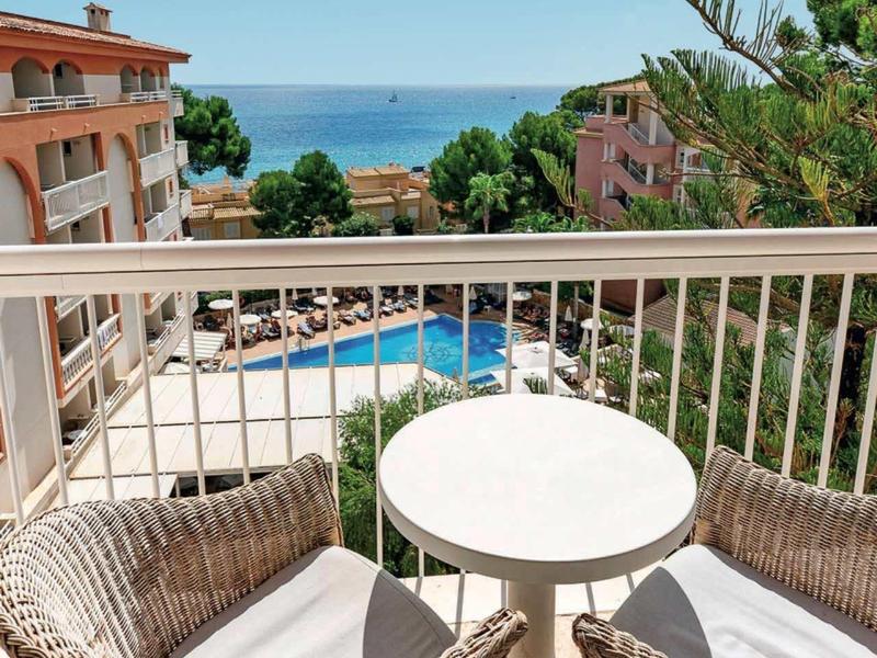 Balcon avec deux chaises et une table avec vue sur la piscine et la mer par un ciel dégagé.