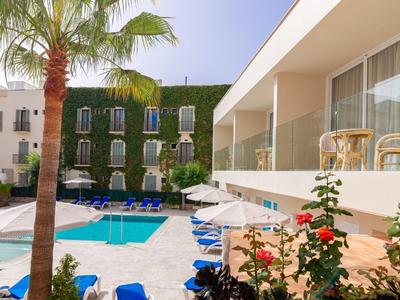 Area piscina all'aperto di un hotel con palme, lettini e architettura moderna.