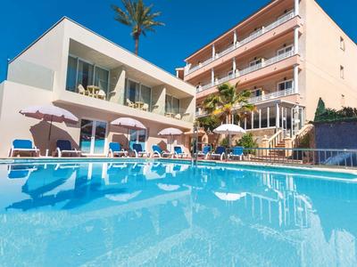 Hotel con piscina, sdraio e ombrelloni davanti a un edificio pluripiano sotto un cielo limpido.