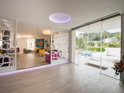 Ingresso moderno dell'hotel con parete in vetro che dà sulla piscina e sul giardino.