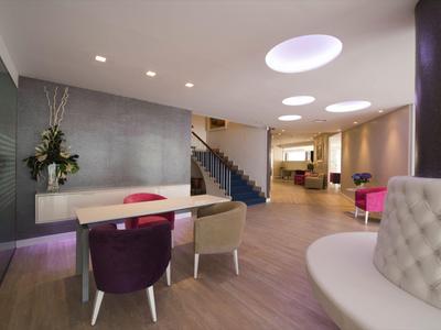 Lobby di hotel moderna con aree salotto, moquette e illuminazione elegante.