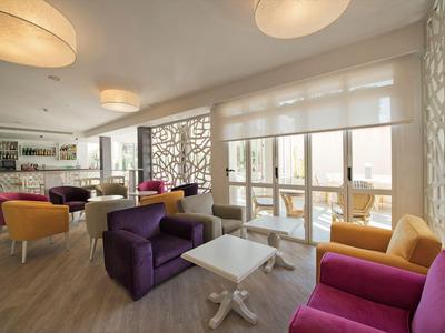 Lounge d'hotel luminosa con poltrone colorate, tavoli bianchi e grandi finestre.