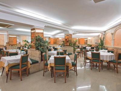 Ampia sala da pranzo con tavoli e sedie, illuminazione luminosa e piante da interno.