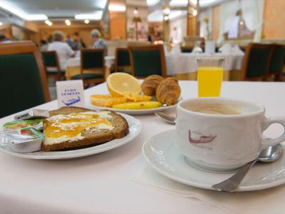 Tavolo apparecchiato per colazione: caffè, toast con marmellata, arance, croissant e succo d'arancia in un ristorante.