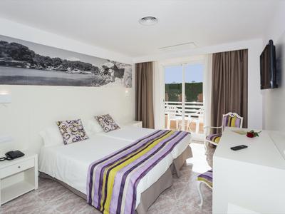 Camera d'hotel moderna con letto matrimoniale, scrivania e balcone con vista su paesaggio verde.