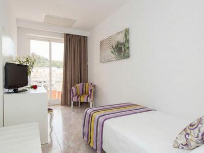 Camera d'hotel luminosa con letto singolo, sedia, TV a schermo piatto e accesso al balcone.