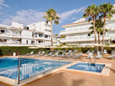 Moderner Hotelpool mit Liegestühlen, Palmen und weißen Gebäuden bei sonnigem Himmel.