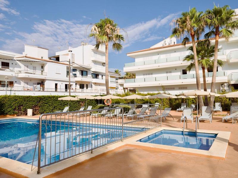 Hotel con piscina all'aperto, lettini e palme sotto un cielo azzurro.