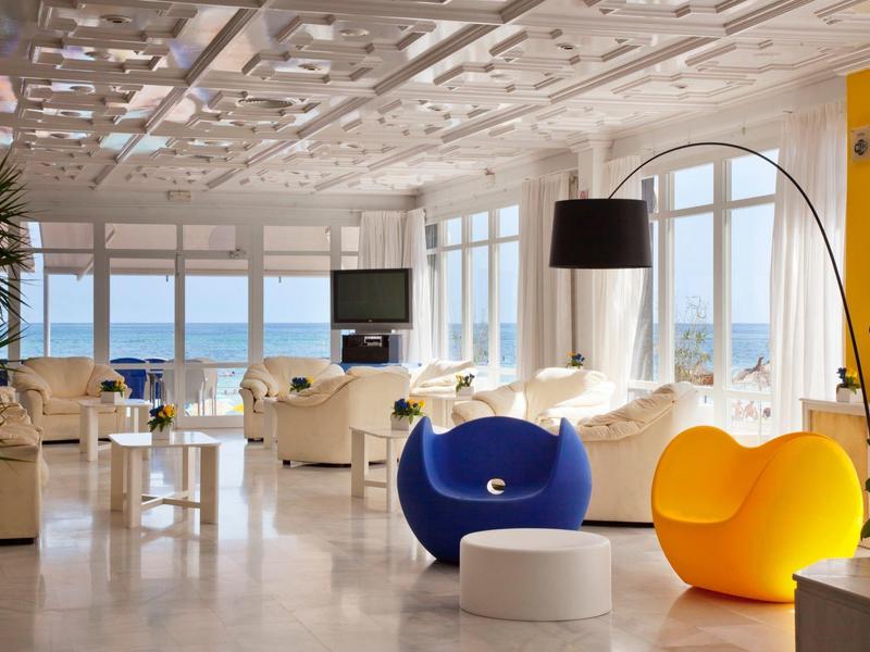 Lounge d'hotel luminosa con sedute colorate e vista mare attraverso grandi finestre