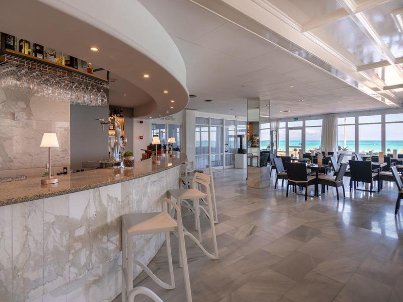 Area bar e ristorante di hotel luminosa e moderna con ampia vista sul mare e sgabelli in legno.