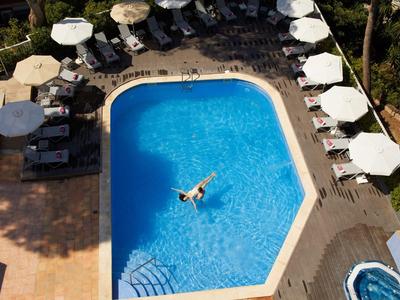Vogelperspektive auf einen blauen Hotelpool mit einer Person und weißen Sonnenschirmen.