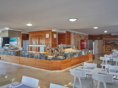 Moderner Frühstücksbereich mit Selbstbedienungsbuffet und weißen Tischen in einem Hotel.