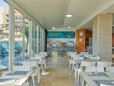 Moderner Speisesaal mit weißen Tischen und Stühlen nahe einem Pool mit Glaswand.