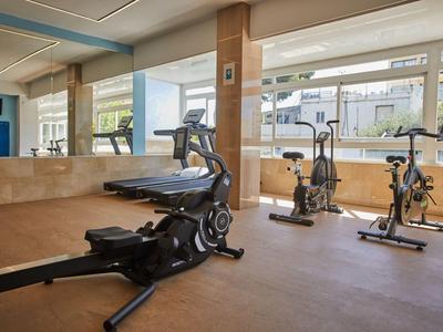 Heller Fitnessraum mit modernen Trainingsgeräten vor großen Fenstern mit Außenblick.