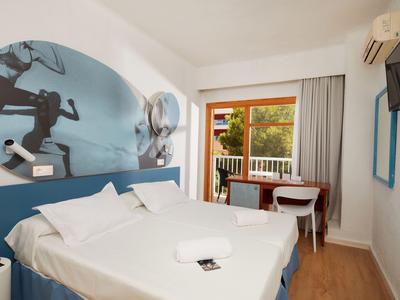 Helles Hotelzimmer mit Doppelbett, Schreibtisch, Balkon und moderner Dekoration in Blau- und Weißtönen.