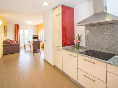 Kuchnia z nowoczesnymi białymi szafkami i czerwoną górną szafką obok otwartej części dziennej z sofą.