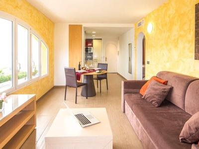 Jasny salon z brązową sofą, stołem jadalnym i kilkoma oknami na żółtej ścianie.