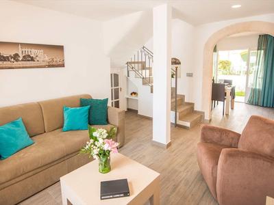 Jasny salon z kanapą, fotelami, schodami i widokiem na jadalnię oraz taras.