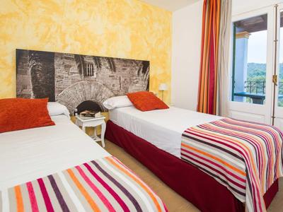 Pokój z dwoma pojedynczymi łóżkami, kolorowymi narzutami i balkonem z widokiem na góry.