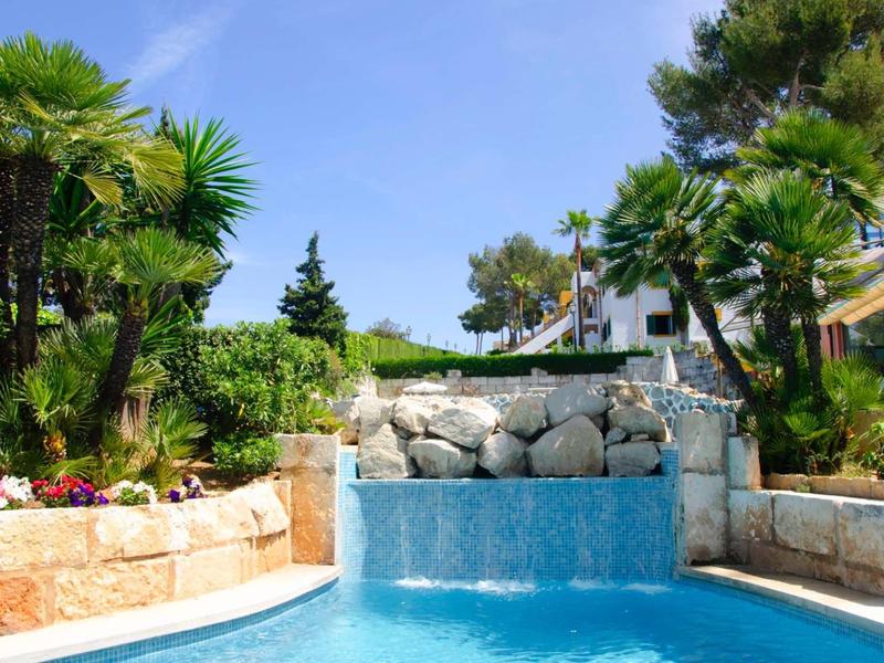 Basen z wodospadem otoczony palmami i roślinami w hotelowym ogrodzie