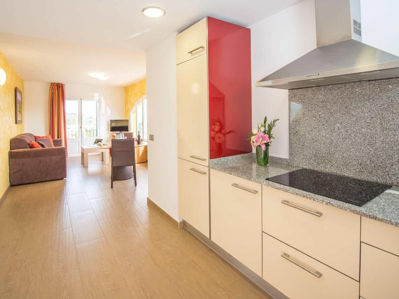 Kuchnia z nowoczesnymi białymi szafkami i czerwoną górną szafką obok otwartej części dziennej z sofą.