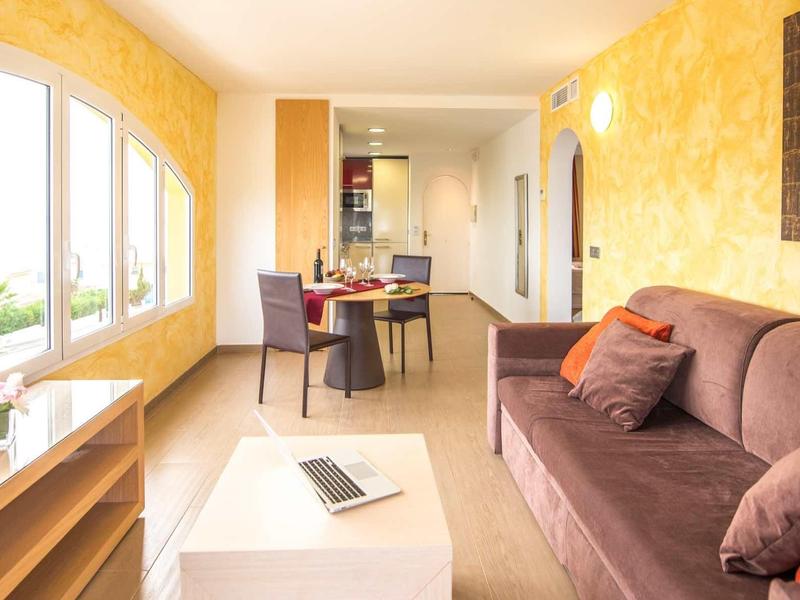 Jasny salon z brązową sofą, stołem jadalnym i kilkoma oknami na żółtej ścianie.