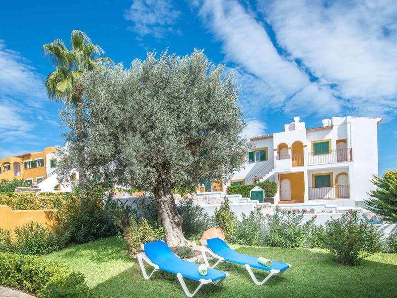 Białe domki wakacyjne z zieloną trawą i niebieskimi leżakami pod niebieskim niebem.