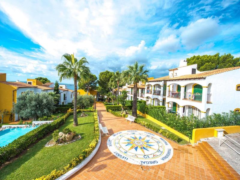 Widok na zadbane ogrody, basen i śródziemnomorskie budynki hotelowe pod niebieskim niebem.