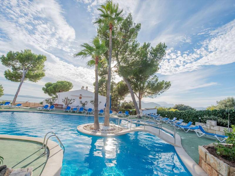 Basen na świeżym powietrzu z palmami, leżakami i błękitnym niebem w ośrodku hotelowym.