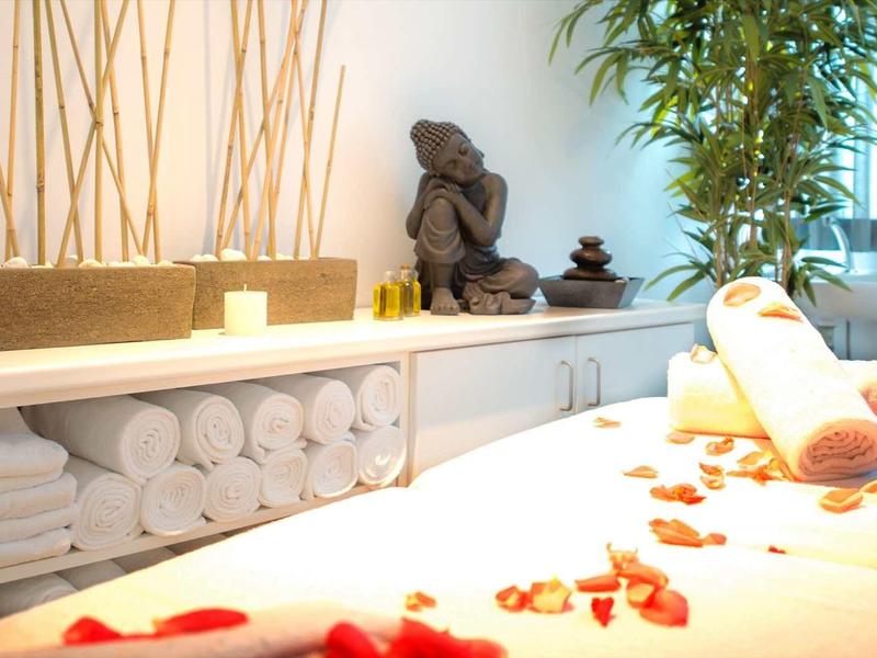 Jasne wnętrze spa z ręcznikami, statuą Buddy i płatkami na stole do masażu