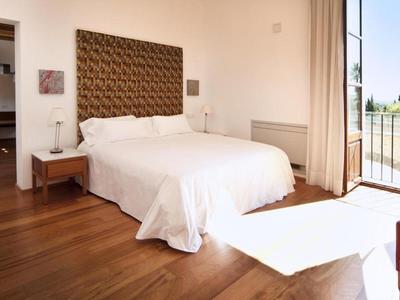 Bright bedroom with double bed, wooden floor, and balcony with view.