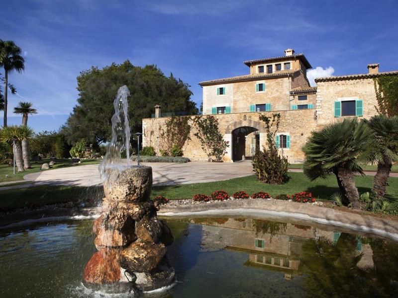 Stone fountain in front of a large Mediterranean-style house with garden.
