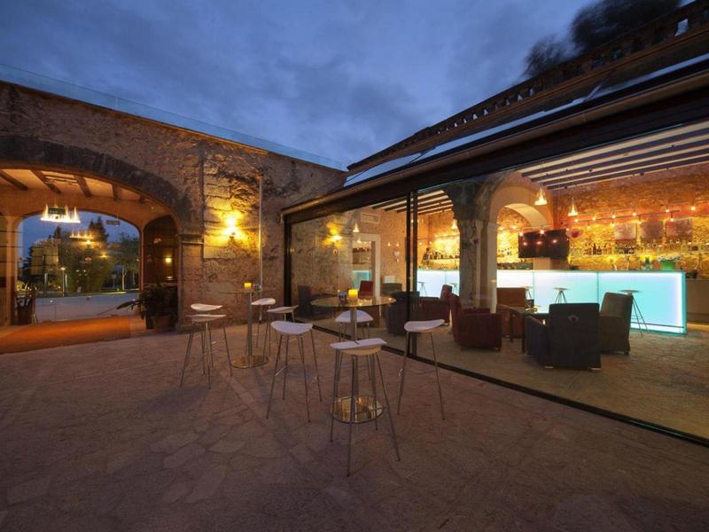 Evening terrace with decoratively lit lounge area and bar in a historic building.
