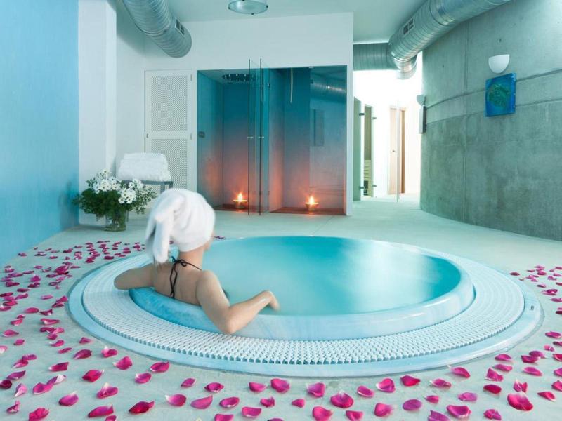 Person relaxing in a jacuzzi surrounded by rose petals in a modern spa area.
