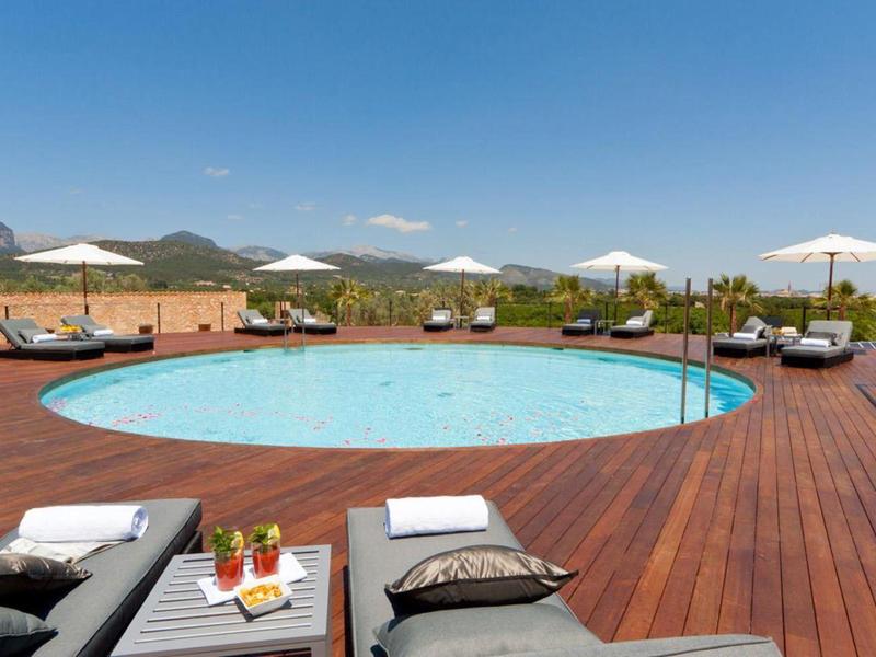 Round pool with wooden deck, loungers, and white umbrellas under blue sky.