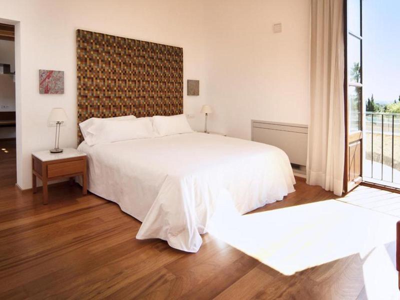 Bright bedroom with double bed, wooden floor, and balcony with view.