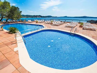 Swimmingpools mit Liegestühlen und Blick auf das Meer bei klarem Himmel.