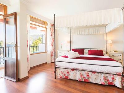 Jasna sypialnia z łóżkiem z baldachimem, balkonem i drewnianą podłogą w pokoju hotelowym.