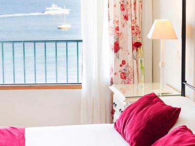 Pokój hotelowy z białym łóżkiem, czerwonymi poduszkami i widokiem na morze przez okno.