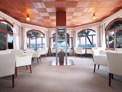 Elegantes Restaurant mit weißen Stühlen und großen Fenstern mit Blick auf ein Gewässer.