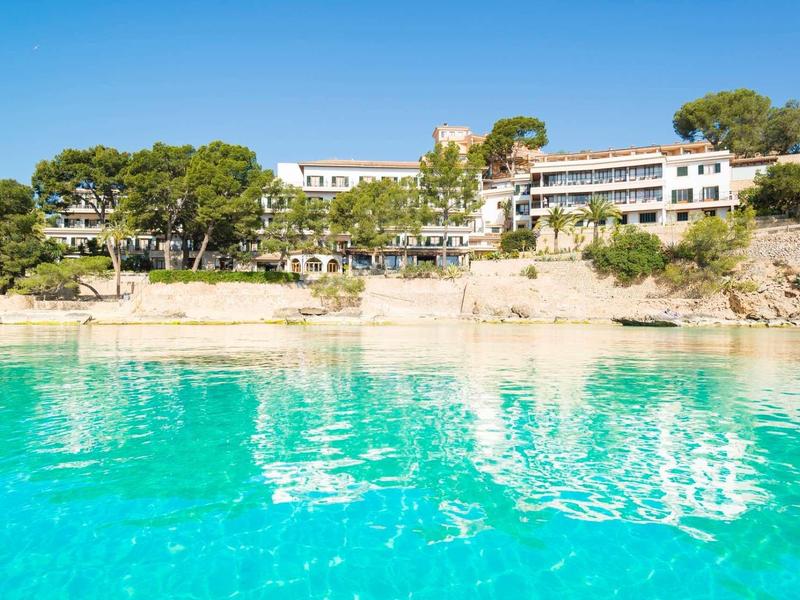 Hotel nad czystą turkusową wodą z skałami i drzewami w tle.